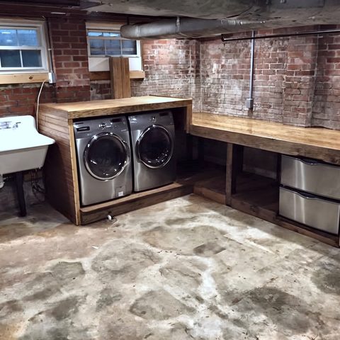 A finished basement laundry with a butcher-block counter, utility sink and exposed brick
