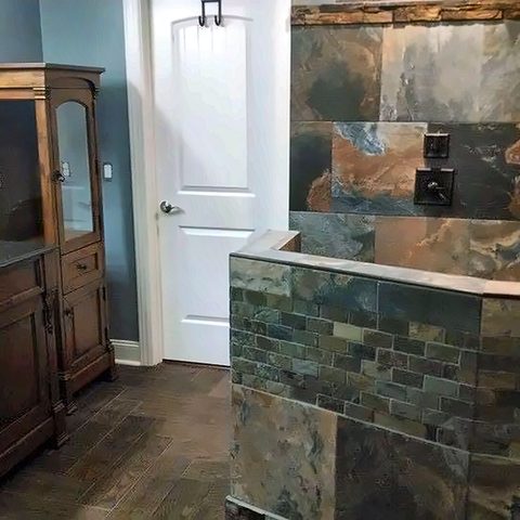 A finished slate-tiled bathroom seen from the hallway, with a tiled half wall