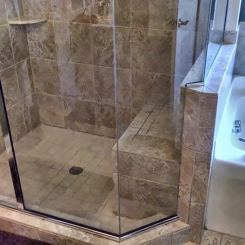 A finished walk-in shower with slate tile, a frameless glass panel and a tiled bench