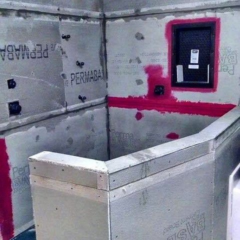 A shower rebuilt in cement board with pink waterproofing membrane sealed into every seam and corner