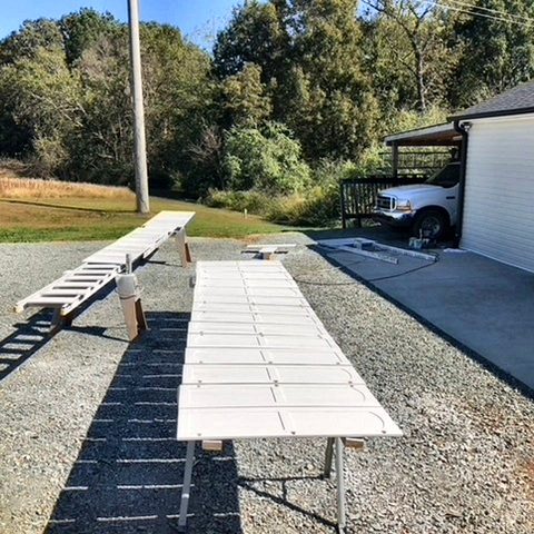 Rows of cabinet doors on folding tables in a driveway after being sprayed white