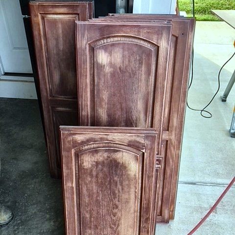 Cabinet doors laid out on a driveway with the old finish sanded back to bare wood