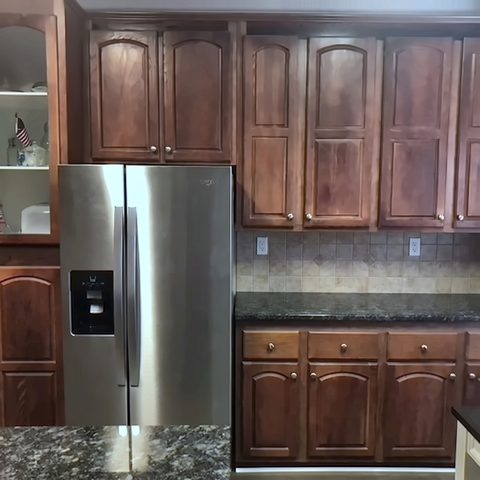 A kitchen before refinishing, with dark cherry raised-panel cabinets, a granite counter and stainless appliances