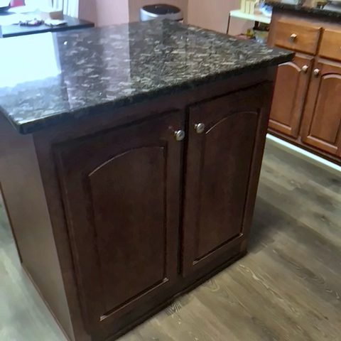 A kitchen island with dark stained cabinets and a speckled granite top