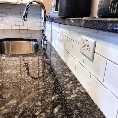A granite counter with an undermount stainless sink, gooseneck faucet and subway-tile backsplash