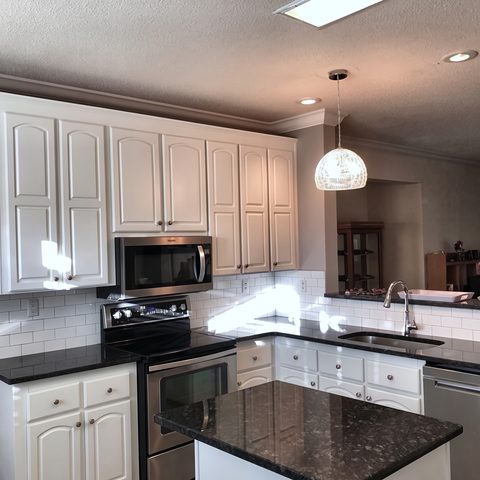 A white kitchen with a black granite island, pendant lighting and stainless appliances