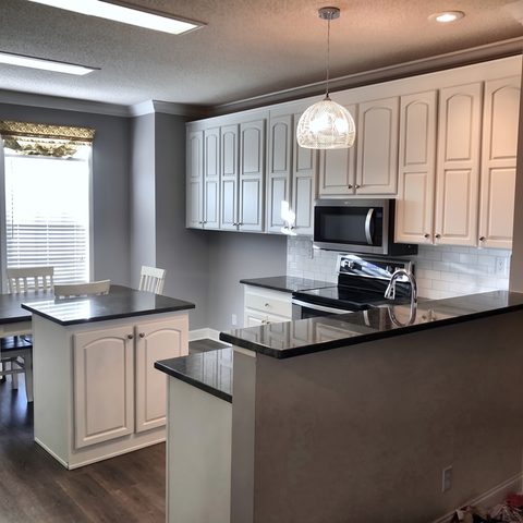 The finished kitchen with white cabinets, black granite counters and a white subway backsplash