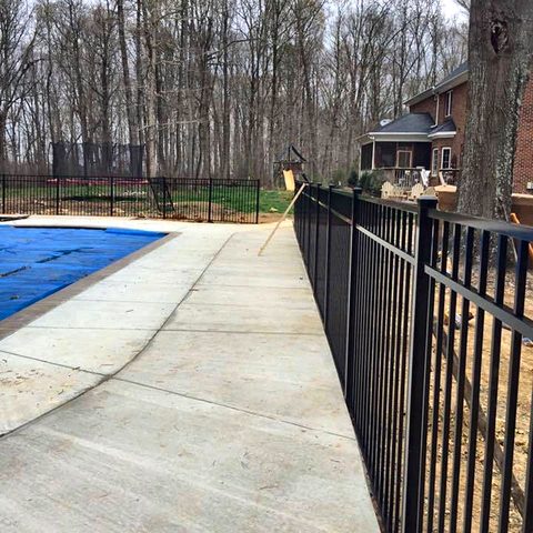A finished concrete pool deck with black metal fencing around it